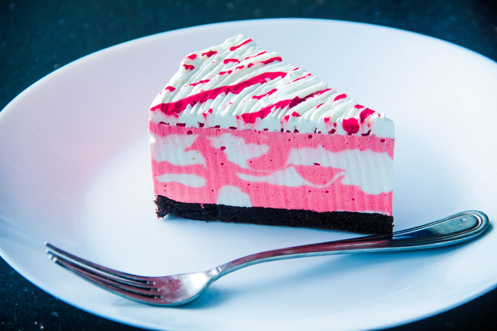 sliced white and pink icing covered cake on white plate with silver colored fork