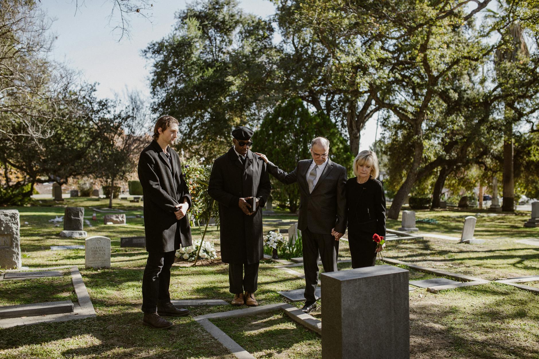 people weraing black and standing over a grave